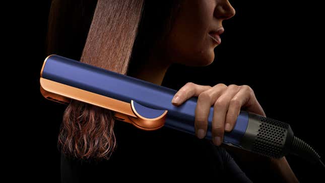 A person with longer hair using the Dyson Airstrait, with a blue finish, to straighten their hair.
