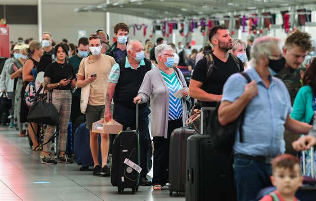 People waiting in line at an airport, many of whom are wearing masks.