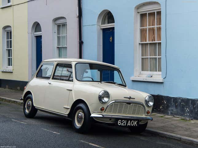 An off-white 1959 Mini is parked in front of pastel old buildings