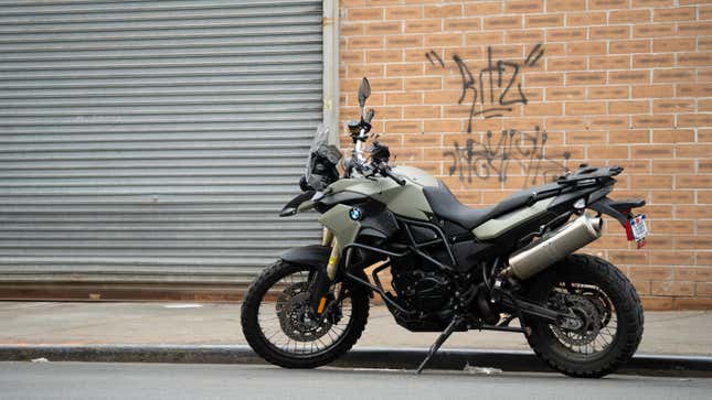 A 2013 BMW F800GS motorcycle, in military green, parked on a road against a red brick building