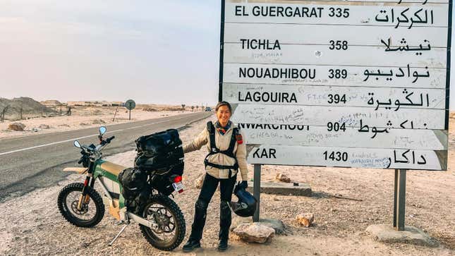 A photo of Sinje Gottwald holding her electric motorcycle next to a road sign. 