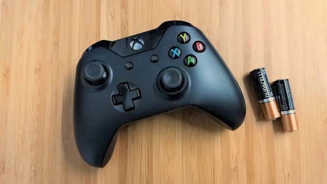 An Xbox One controller appears on a table next to batteries. 