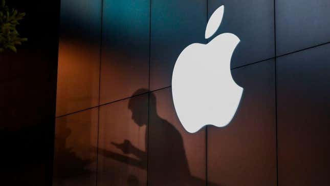 A silhouette of a man using an iPhone in front of the Apple logo.