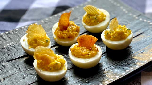 Deviled eggs with a potato chip garnish on a black plate