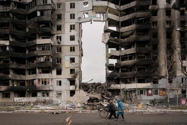 Two women walk past a apartment complex with a massive hole in its center in Ukraine.