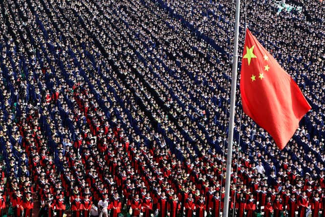 A bird's eye view of a sea of graduates standing in columns with a Chinese flag in the foreground.