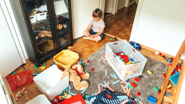 young child sitting in a room with toys scattered across the floor