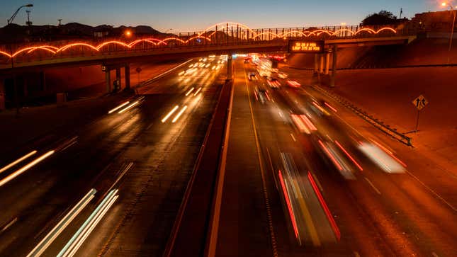 A photo of a highway at sunset with cars zooming past. The tail lights are blurred. 