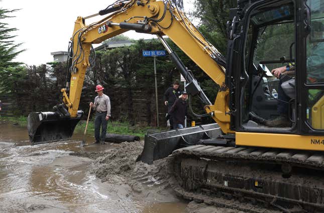A Marin County firefighter looks on as a backhoe removes sand from a street after large waves flooded a neighborhood on January 05, 2023 in Stinson Beach, California.