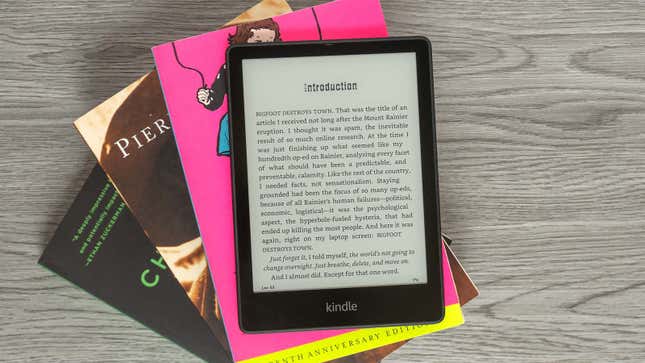 The Amazon Kindle Paperwhite 5 sitting atop a pile of books on a desk.