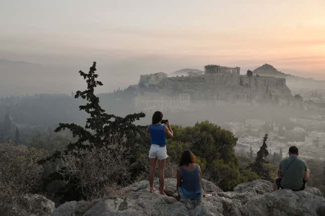 Onlookers take pictures of smoke covering Athens, with the Acropolis in the background.