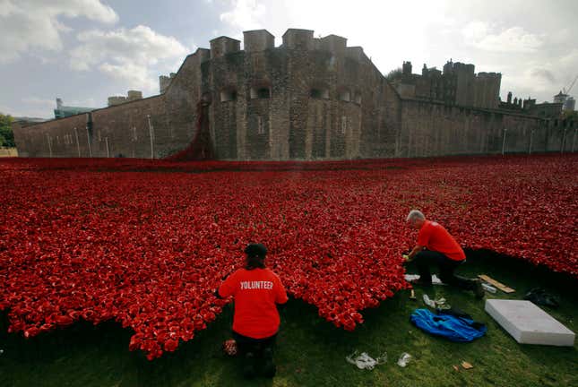 Volunteers plant ceramic poppies amongst other poppies that form part of the art installation called "Blood Swept Lands and Seas of Red" at the Tower of London October 9, 2014. The evolving art installation, which will be completed on November 11, will create a commemoration for the centenary of World War One. REUTERS/Luke MacGregor (BRITAIN - Tags: MILITARY SOCIETY TRAVEL ANNIVERSARY) - RTR49IXP