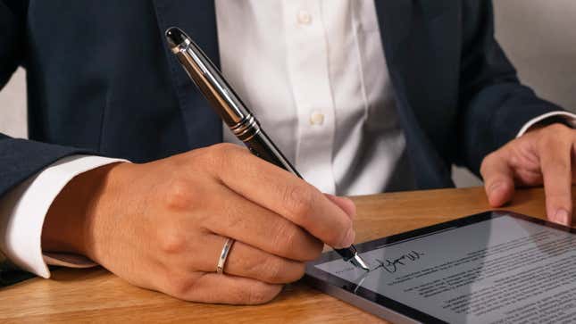A person in a suit signing their name on a tablet device on a desk using the Adonit Star stylus which looks like a fountain pen.