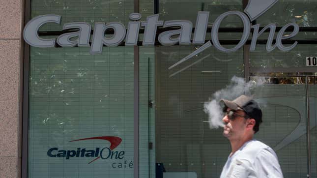 A man smokes a cigarette outside a building with a capital one logo and capital one cafe logo on the side.