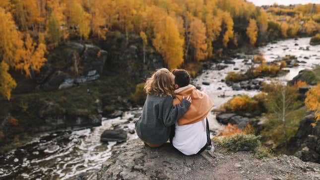 Couple sitting on rock next to creek and fall foliage 