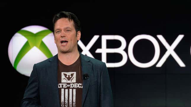 Head of Xbox Phil Spencer stands in front of an Xbox sign wearing a State of Decay shirt. 