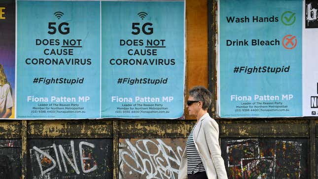 A woman walks past posters debunking the 5G conspiracy theory causes covid-19