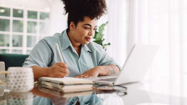 Woman working at laptop, taking notes. 