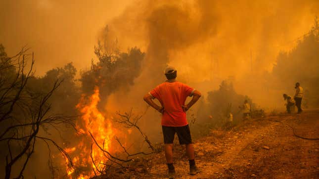 A volunteer watches as firefighters use a water hose to extinguish the blaze of a forest fire in the village of Glatsona on Evia (Euboea) island, on August 9, 2021. 