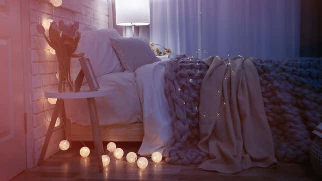 A dim room with a cozy looking bed covered in blankets, with low lighting provided by a string of small globe lights