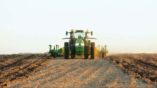 A green John Deere self-driving tractor plows a field. 