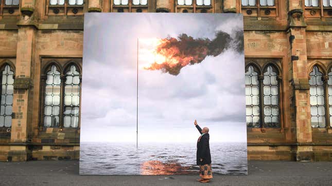 Tongan artist and climate activist, Uili Lousi, is seen with a blown up version of John Gerrards "Flare Oceania 2021," a piece of art depicting a gas flare above the ocean.