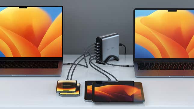 The Satechi 200W 6-Port PD GaN Charger standing upright on a desk while connected to two smartphones, two tablets, and two laptops, with six USB-C cables.