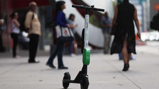 A lime scooter on the sidewalk with people walking by in the background.