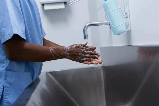Mid section of African-american male surgeon washing hands in sink at hospital. Shot in real medical hospital with doctors nurses and surgeons in authentic setting