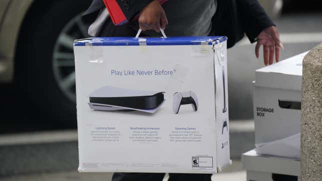 A woman carries a Playstation PS5 box as she arrives at federal court surrounded by white storage boxes and a car