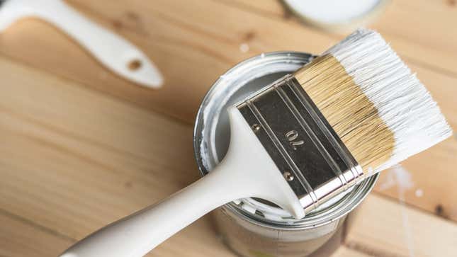 A paintbrush dipped in white paint renting on a can of paint