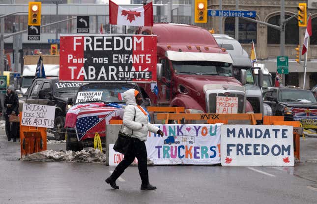 A woman crosses the street in front of vehicles parked as part of the trucker protest, Tuesday, Feb. 8, 2022 in Ottawa. Canadian lawmakers expressed increasing worry about protests over vaccine mandates other other COVID restrictions after the busiest border crossing between the U.S. and Canada became partially blocked.
