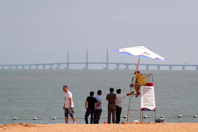 Visitors chat with a lifeguard on a beach as they look at the Zhuhai-Macau-Hong Kong Bridge in Zhuhai in south China’s Guangdong province.