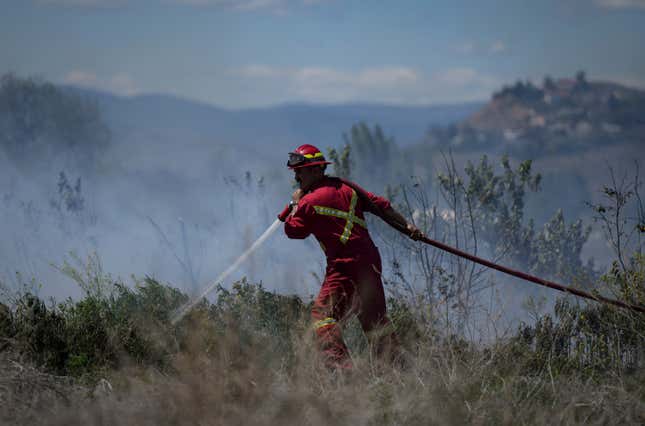 A firefighter directs water on a grass fire on an acreage behind a residential property in British Columbia, on June 5, 2023.