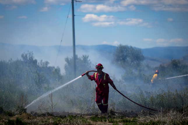 A firefighter directs water on a grass fire burning on an acreage behind a residential property in British Columbia, Canada, on June 5, 2023.