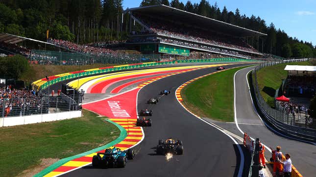 A photo of Formula 1 cars racing up a corner on a race track. 