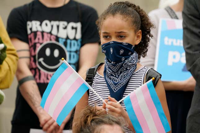 A young child holds a pair of trans pride flags at a noon gathering on the steps of the Mississippi Capitol in Jackson, as they protest House Bill 1125, which bans gender-affirming care for trans children, Wednesday, Feb. 15, 2023