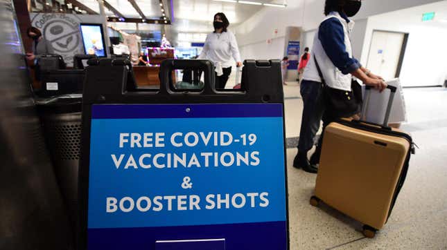 Travelers walk past a sign offering free Covid-19 vaccinations and booster shots at a pop-up clinic in the international arrivals area of Los Angeles International Airport in Los Angeles, California on December 22, 2021.