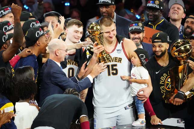 Jun 12, 2023; Denver, Colorado, USA; NBA commissioner Adam Silver presents the Bill Russell NBA Finals MVP Award to Denver Nuggets center Nikola Jokic (15) as Jokic holds his daughter Ognjena Jokic after the Nuggets won the 2023 NBA Championship against the Miami Heat at Ball Arena. Looking on is Denver guard Jamal Murray (27) holds the Larry O&#39;Brien Trophy.