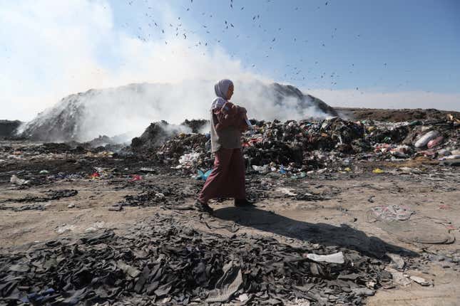 A woman carrying a child walks through a landfill in the outskirts of Bishkek, Kyrgyzstan
