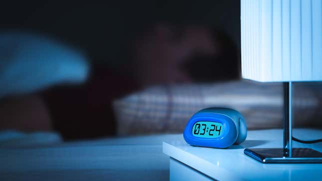 close-up of a digital clock at night, person sleeping in background
