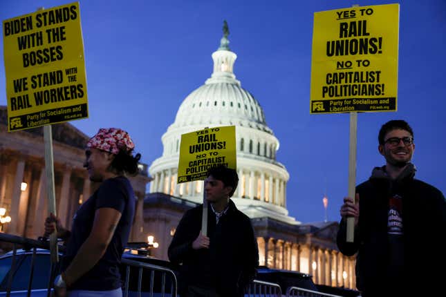 Three activists stand in front of the US Capitol building. They hold signs reading, "Yes to rail unions! No to capitalist politicians!" and "Biden stands with the bosses, we stand with the rail workers."