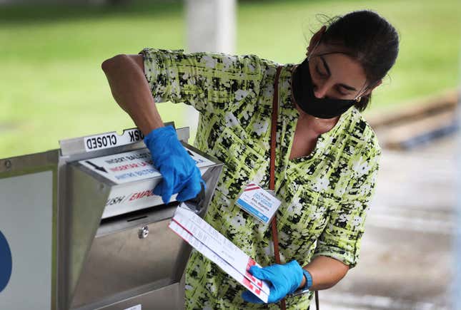 A poll worker places Vote-by-Mail ballots into an official ballot drop box set up at the Election Headquarters polling station on October 19, 2020, in Doral, Florida.