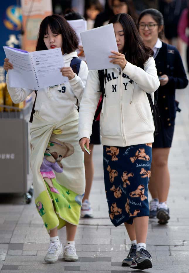 Two high-school seniors walk while studying, in front of Pungmun Girls High School in Seoul in October 2015.