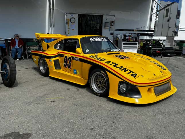 A yellow Porsche 935 race car is parked in the pits at Laguna Seca
