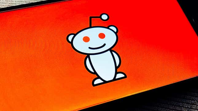 Reddit's smiling Alien logo, named Snoo, is shown against an orange backdrop on a phone.