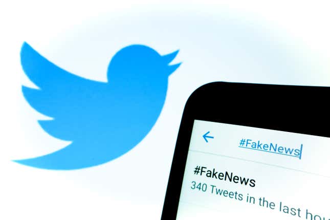 A phone with #FakeNews written in the search bar with the Twitter bird logo in the background.