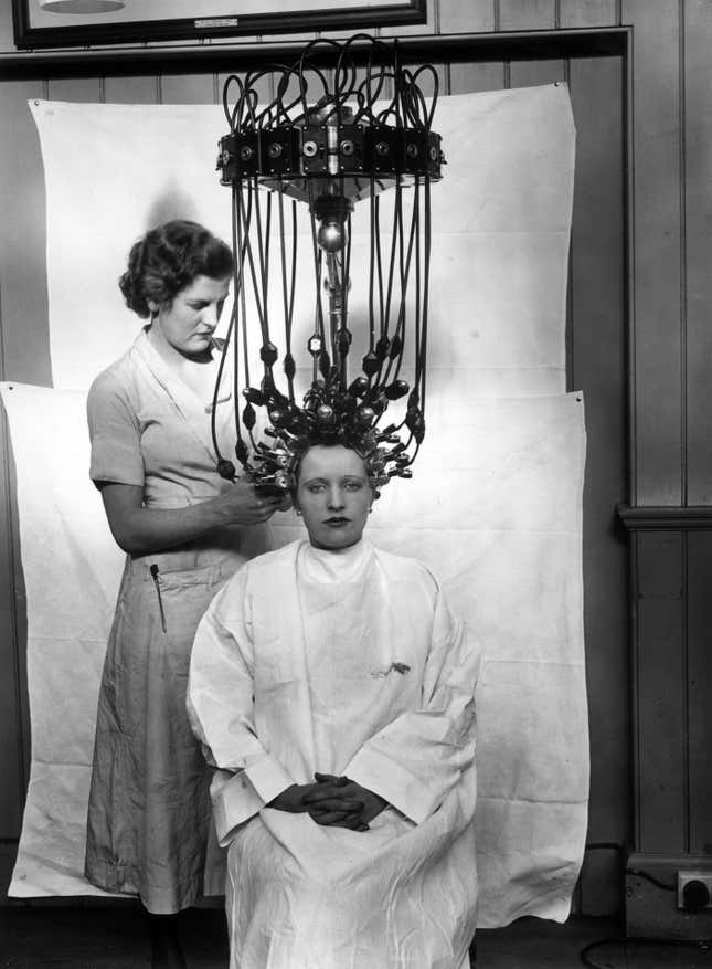 A woman using a perming machine made by Messrs Gallia.
