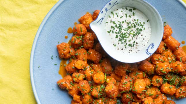 A light blue plate of Buffalo tater tots with a side of ranch sits on a yellow tablecloth