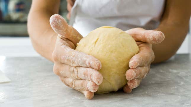 Hands shaping ball of dough on countertop